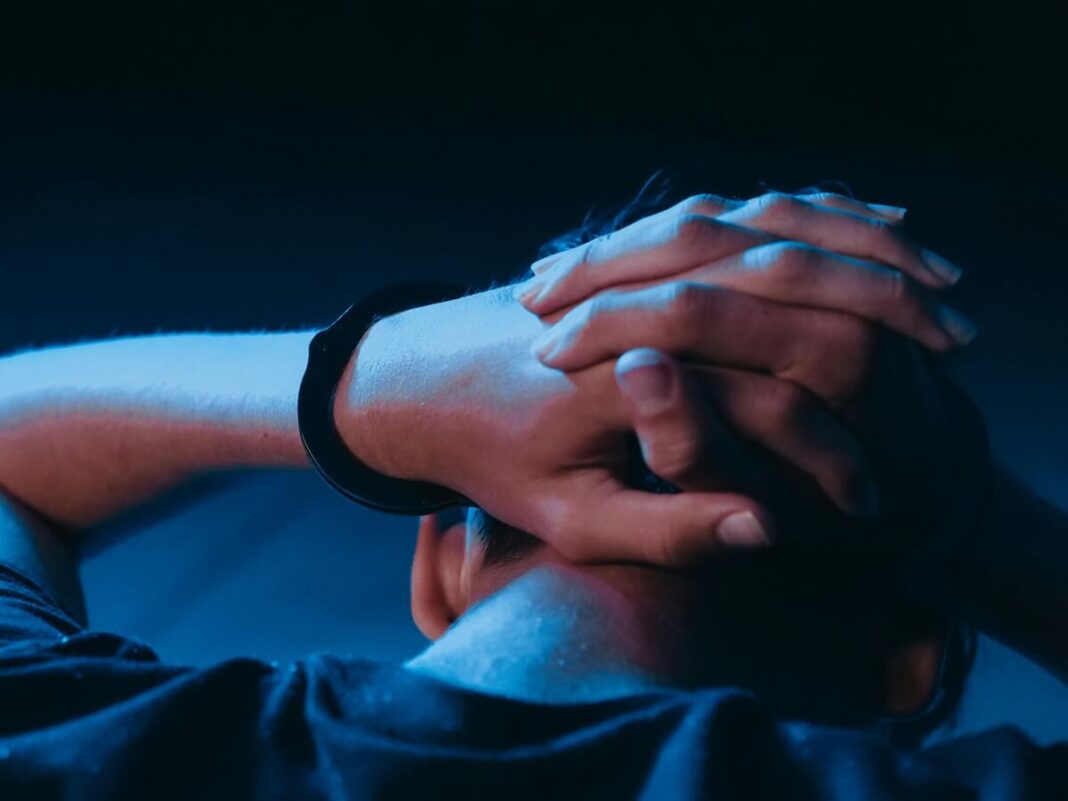 boy facing away with hands on his head in one handcuff