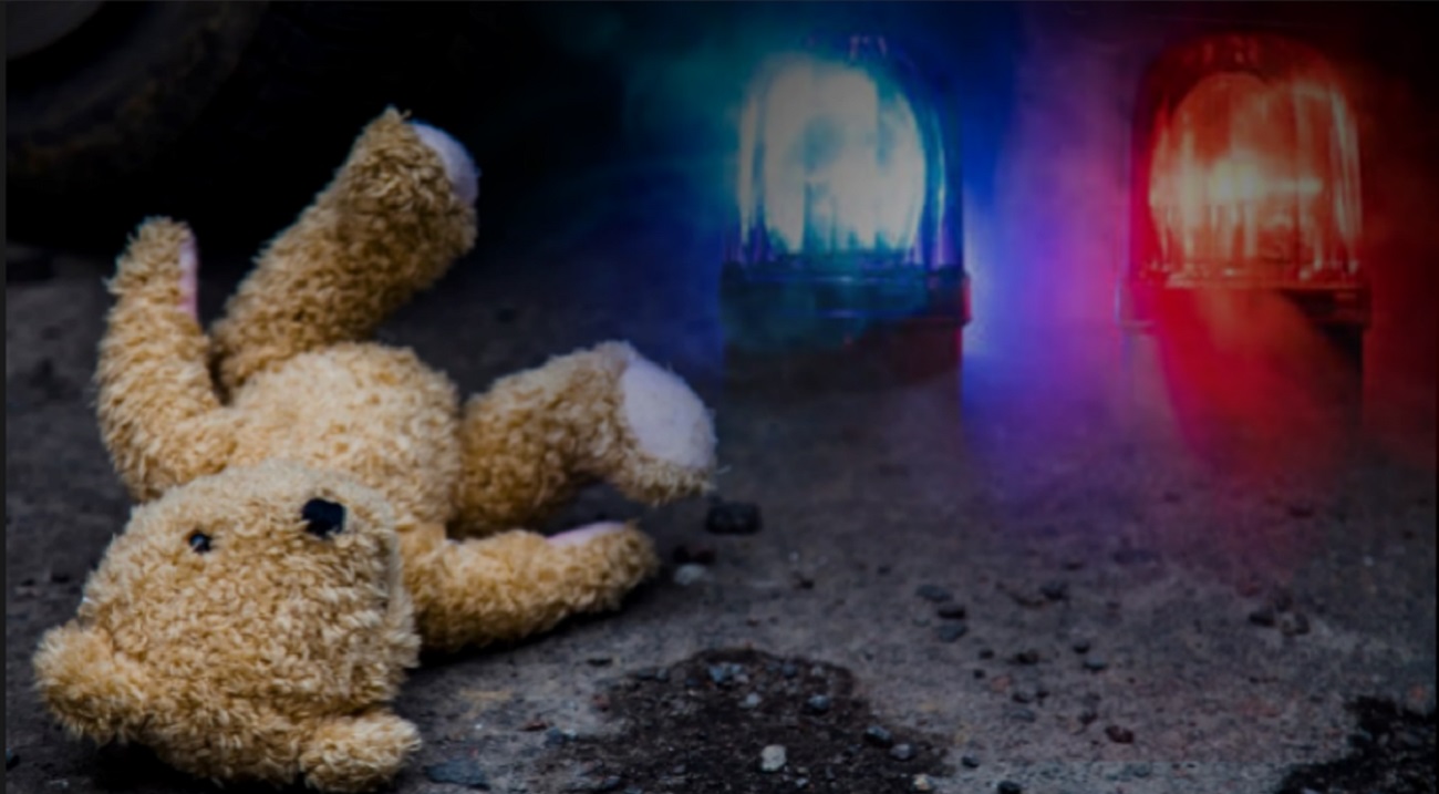 A teddy on the ground with emergency lights in the background